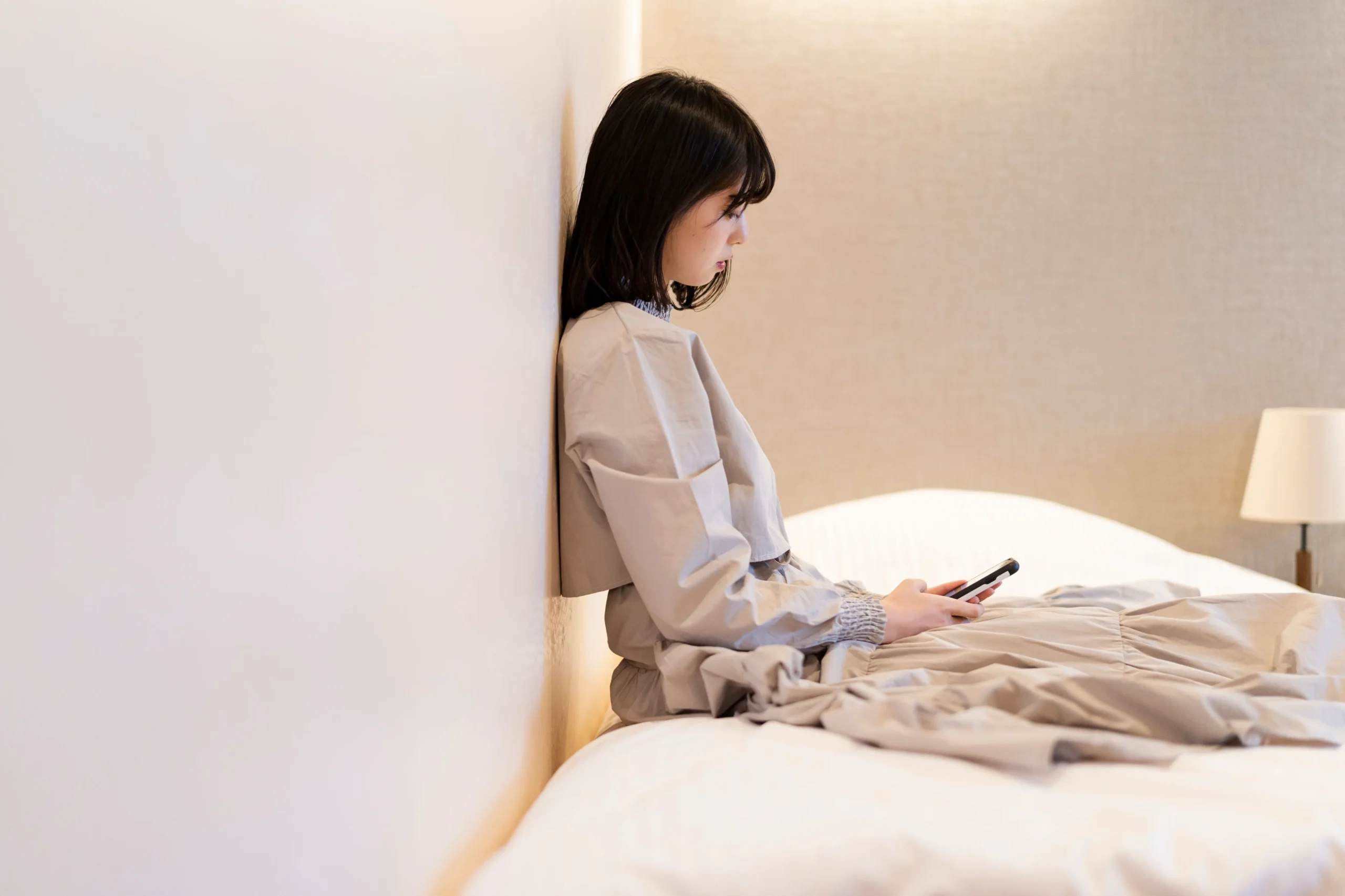 寝室でスマートフォンを使う女性